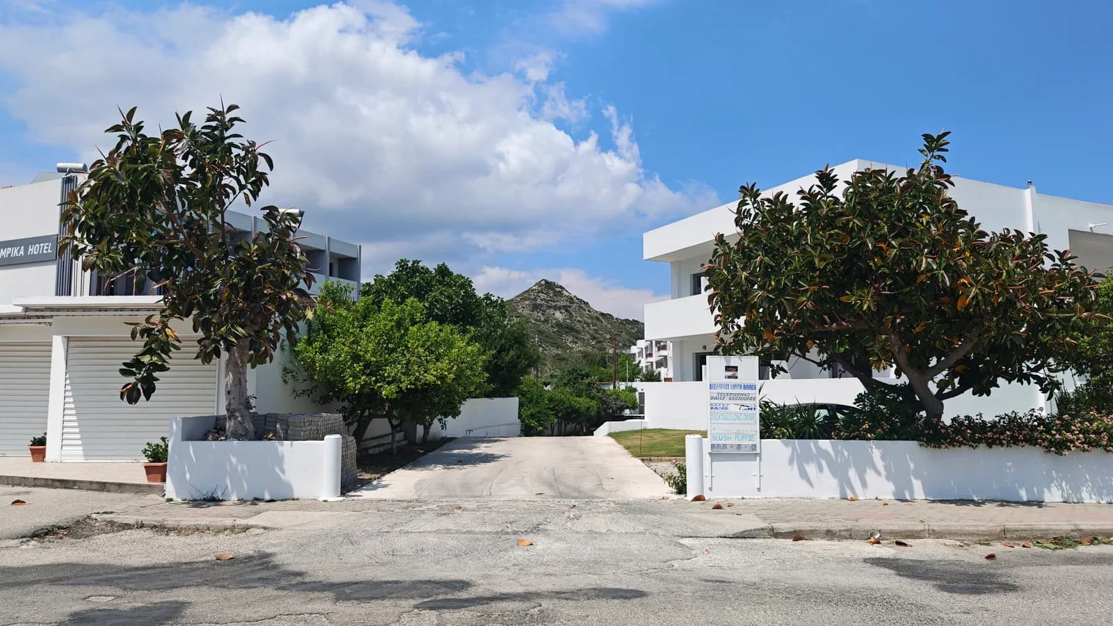 Otoczenie hotelu na Rodos z białą zabudową, zielenią i lokalną ulicą